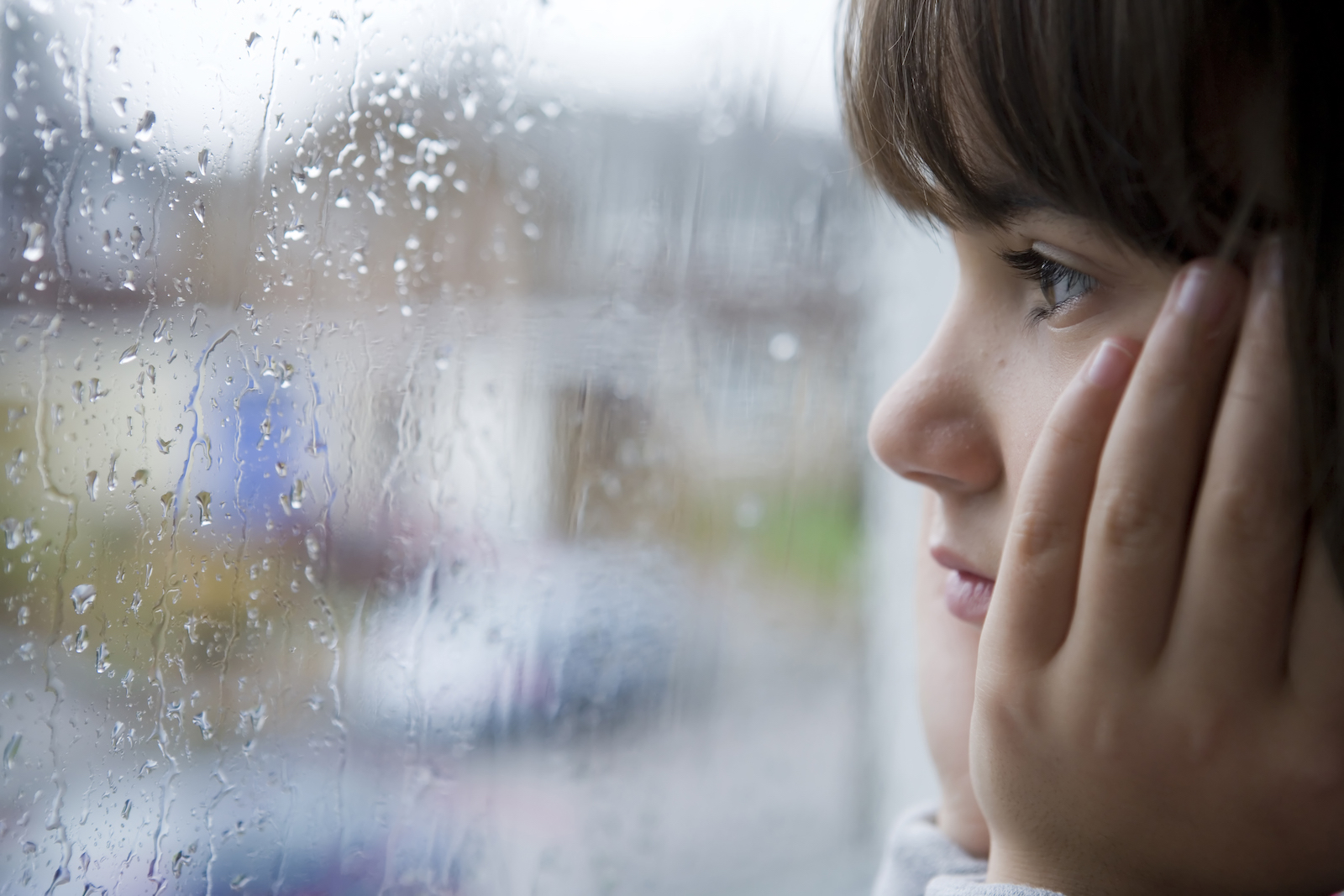 young child looking out of window on rainy day